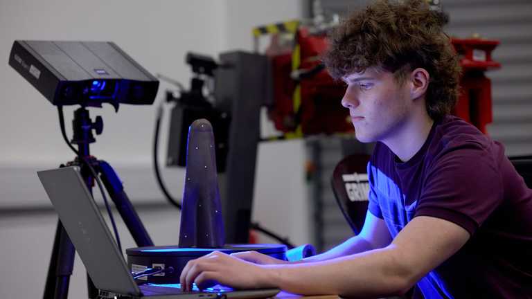 A student's face lit up by a computer as he looks at scans of machinery