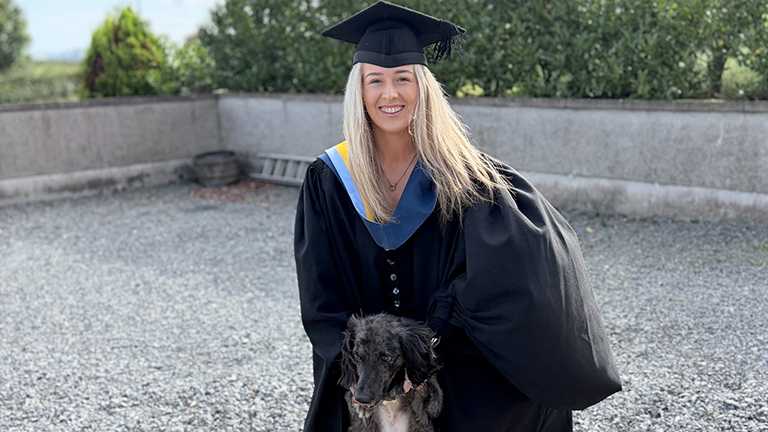 A young woman - Lauren McGee - in a graduation gown with a dog