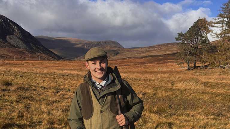 A man - Tom Ewin 0 in country sportswear in a mountain glen