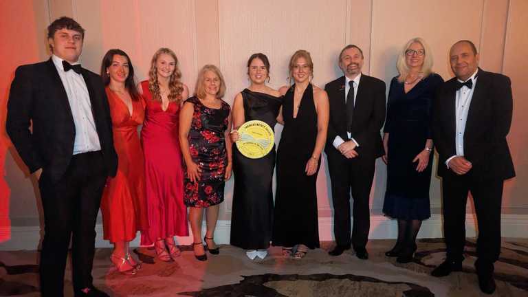 Emma Burgess holds her award flanked by fellow graduates, students and lecturers