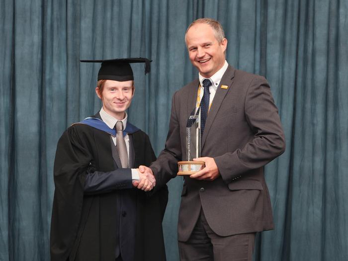 Carl receives the award from Trophy from Simon Wood, Technical Excellence Leader at JCB