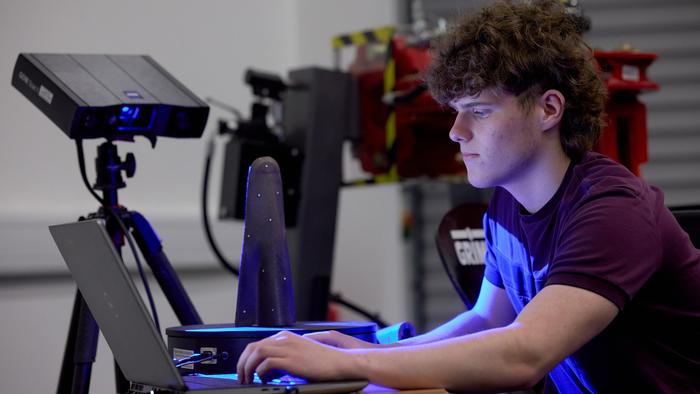 A student's face lit up by a computer as he looks at scans of machinery