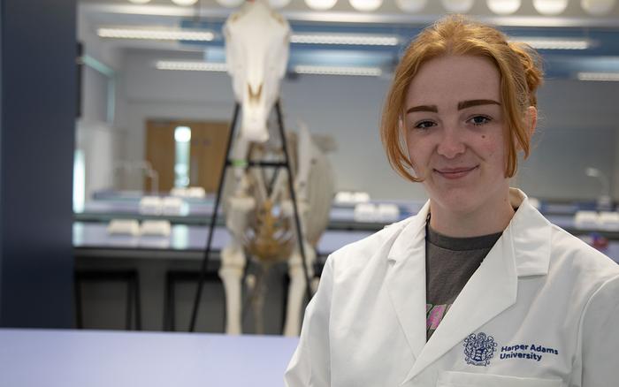 A woman - Martha Stokes - in a white lab coat with a hore skeleton behind her.