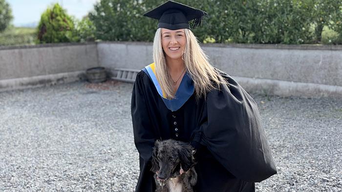 A young woman - Lauren McGee - in a graduation gown with a dog