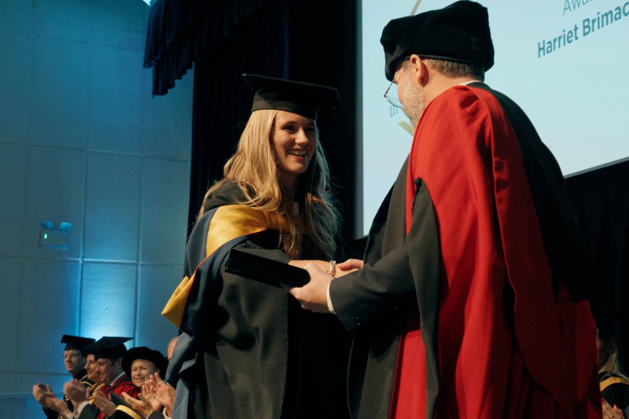 Harriet wearing graduation gown and cap accepting an award from Professor Michael Lee.